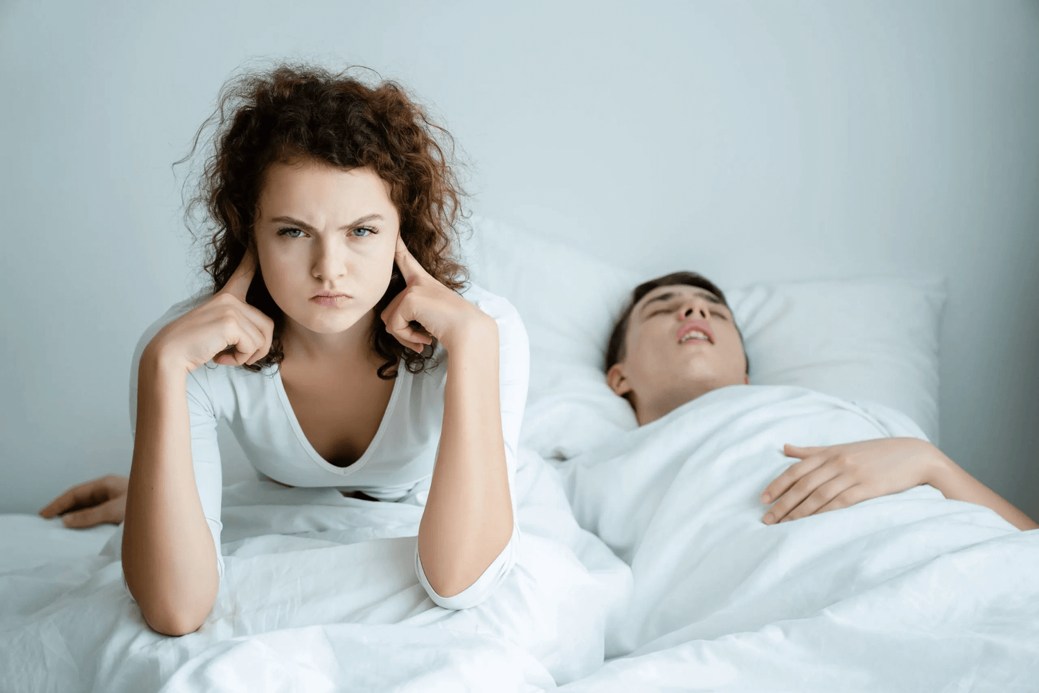 Frustrated woman awake in bed next to snoring partner, highlighting the need for snoring prevention solutions like smart pillows.