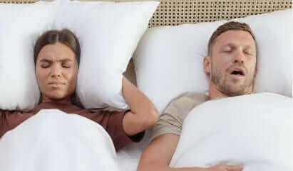 Couple in bed with woman uncomfortable due to snoring, highlighting sleep quality issues.