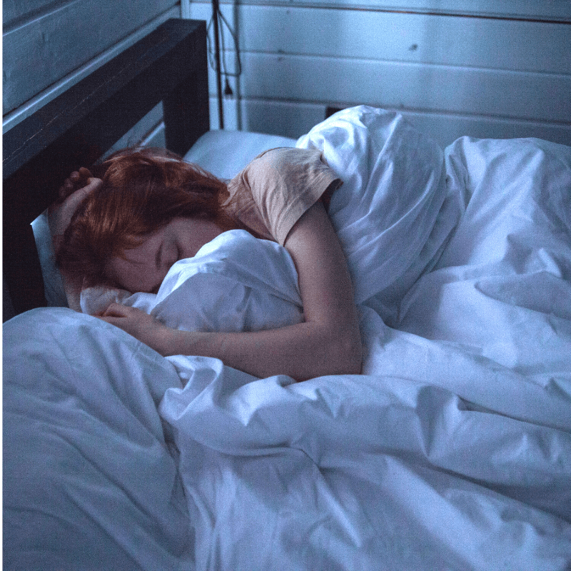 Woman sleeping peacefully on bed, illustrating restful sleep with smart pillow solution for snoring issues.