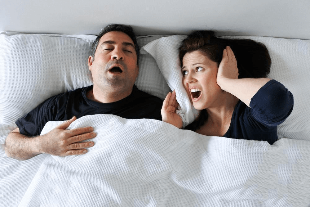 Woman disturbed by partner's snoring in bed, highlighting need for anti-snoring solutions like Nitetronic's pillow.