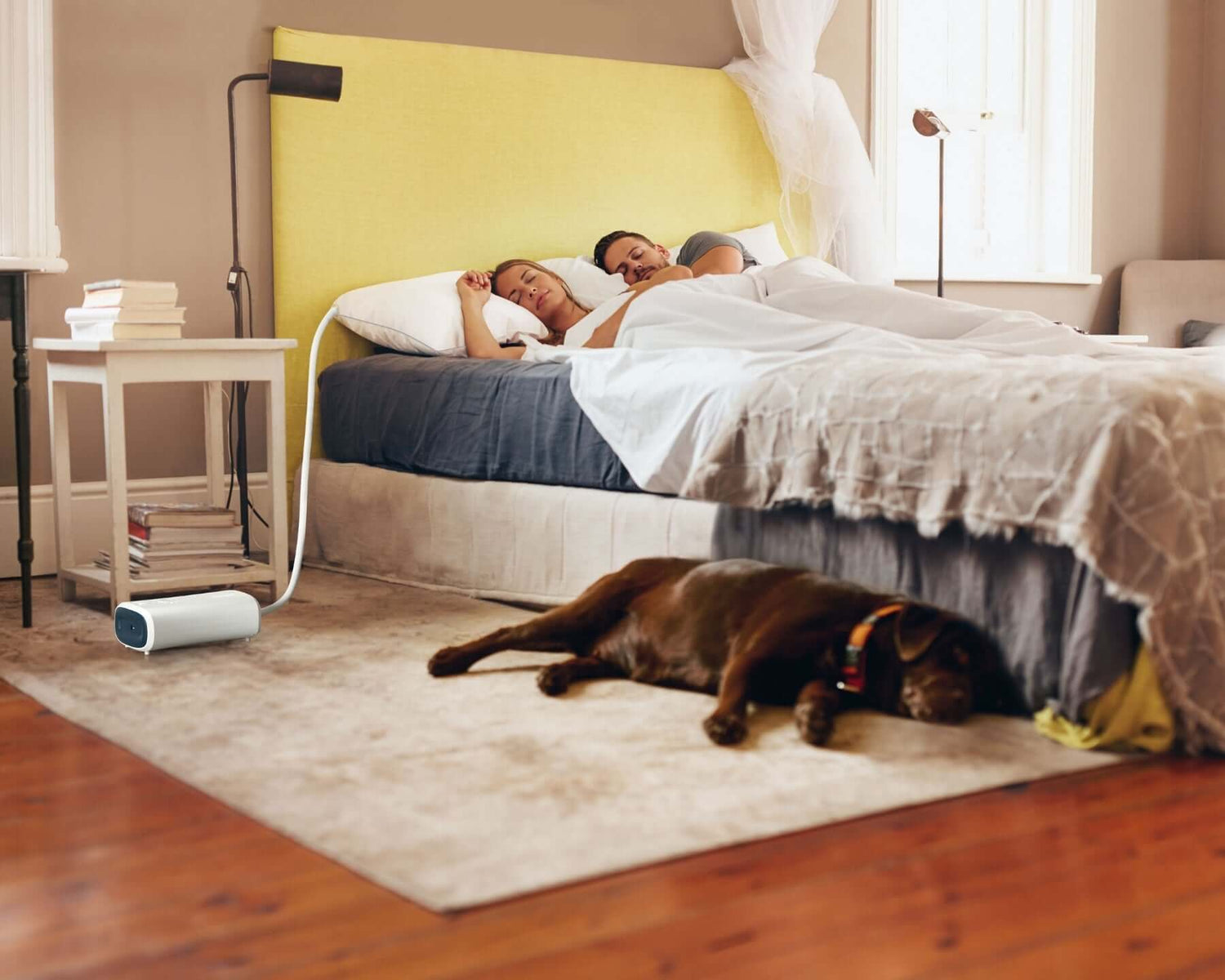 Couple sleeping on a bed with a smart anti-snore pillow, enhancing sleep quality; a dog lies on the floor in a cozy bedroom.