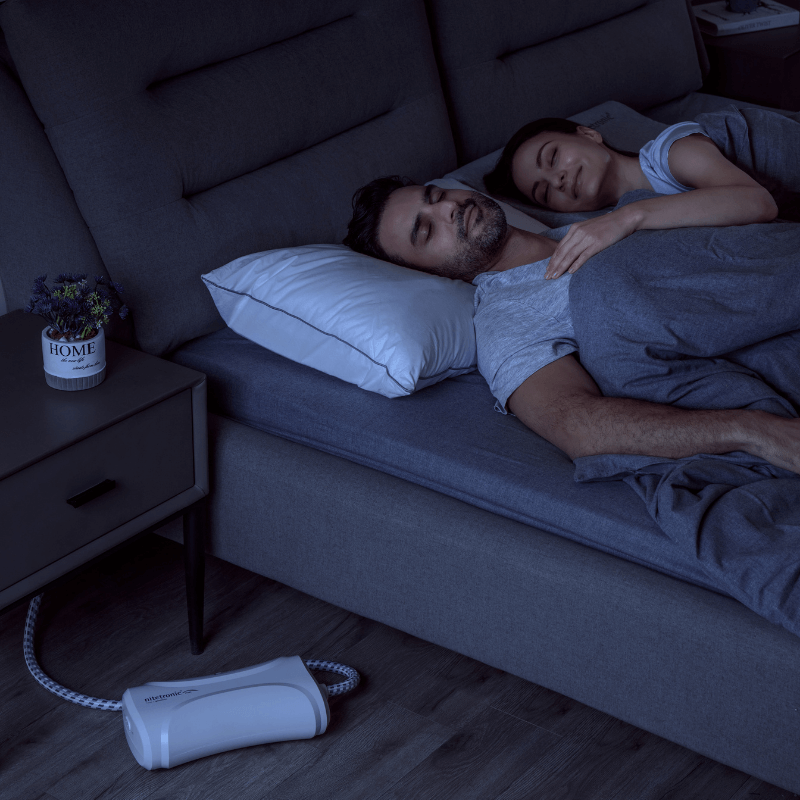Couple sleeping peacefully on a bed with an anti-snoring pillow and device, highlighting sleep solutions for interrupted sleep.