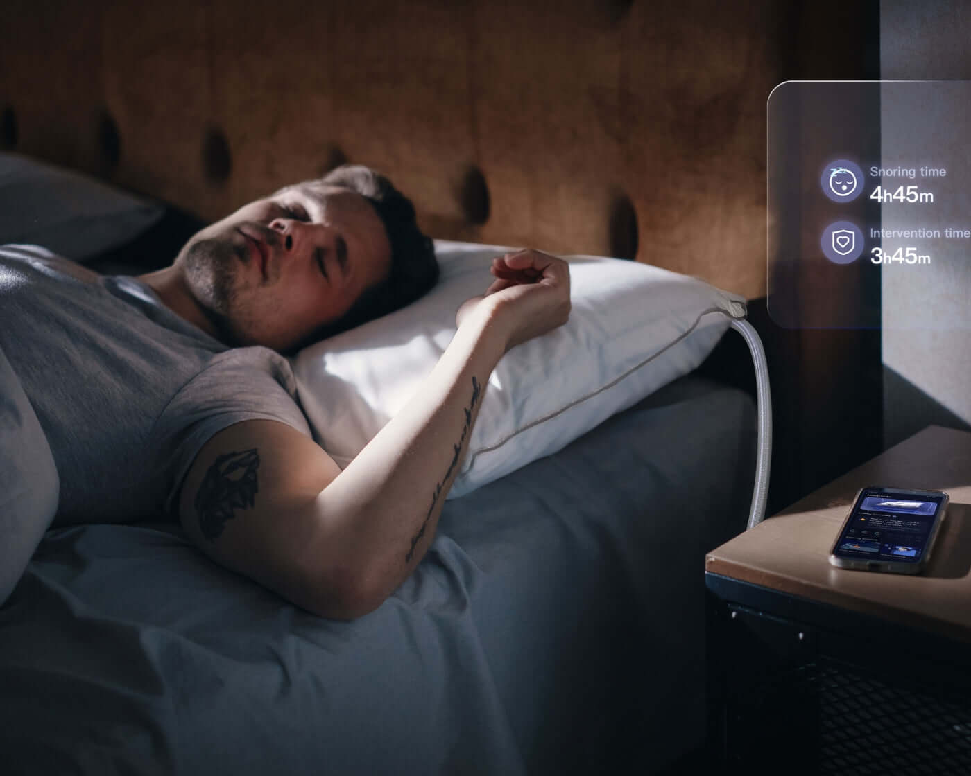 Man sleeping on Nitetronic anti-snore pillow for sleep apnea comfort, with sleep monitoring app by bedside.