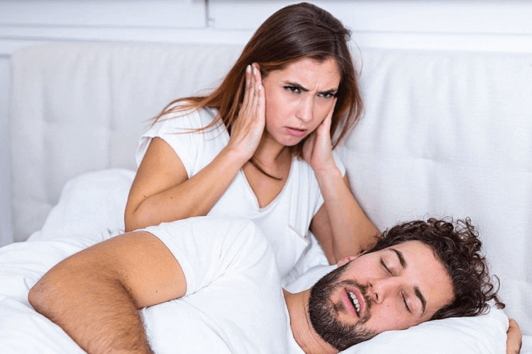 Woman frustrated by partner's snoring while sleeping, highlighting the need for anti-snore solutions like the Nitetronic Z6 pillow.