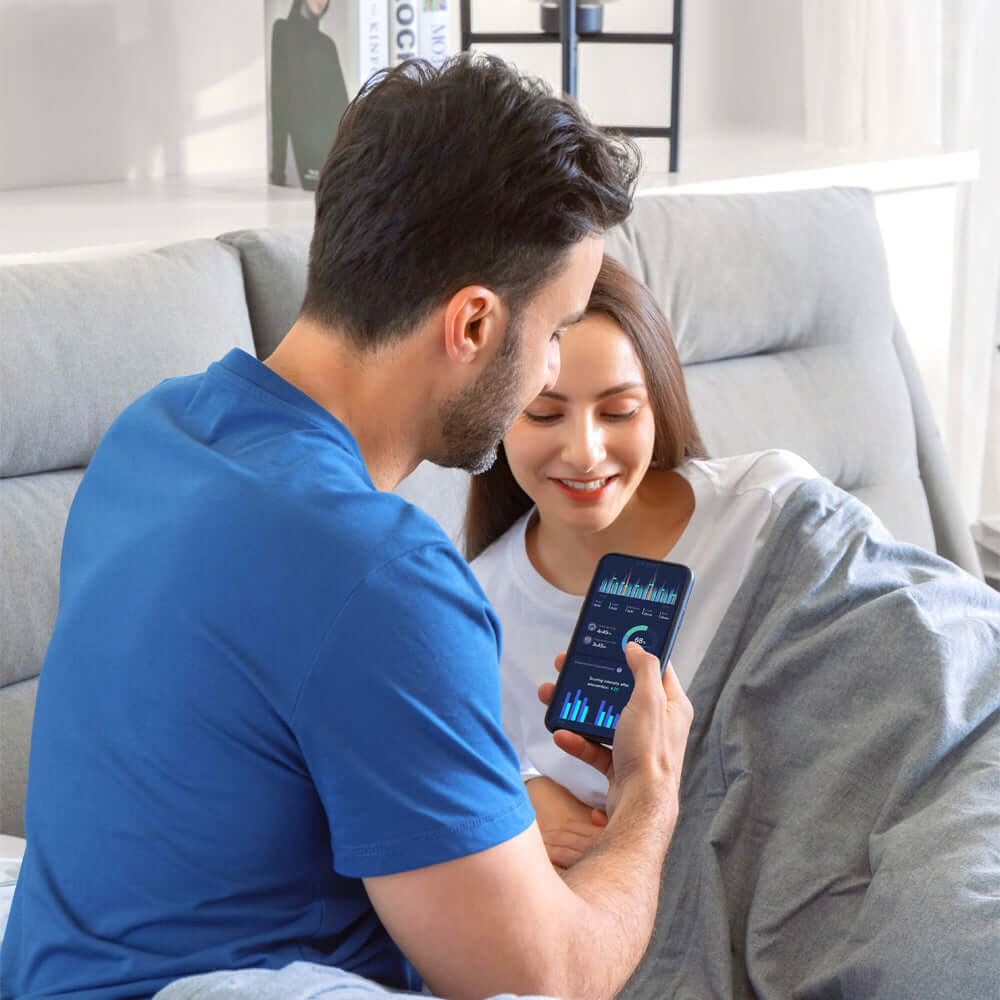 Couple using sleep tracking app in bed with anti-snore pillow, discussing sleep quality improvement.