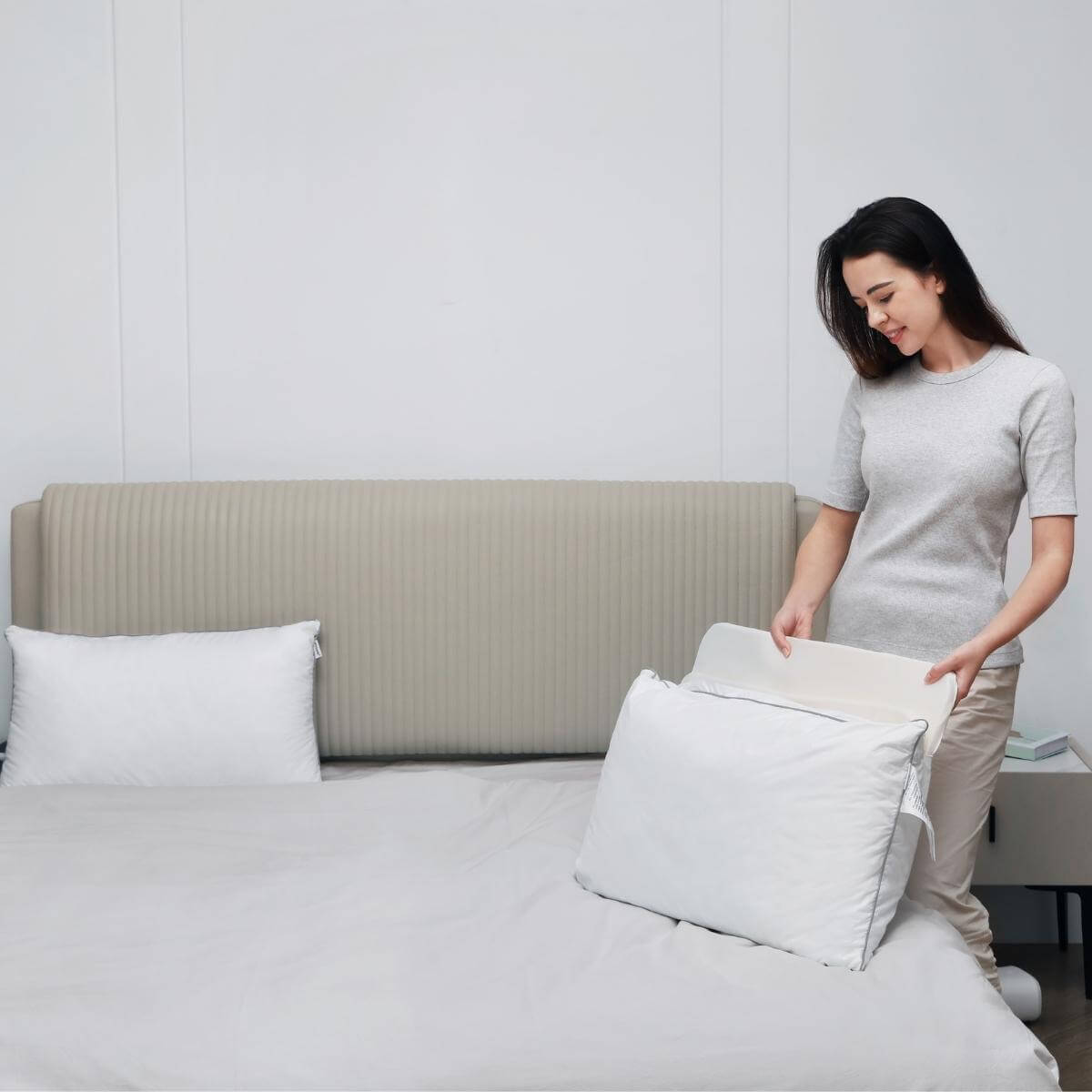 Woman setting anti-snore pillow on bed in modern bedroom.