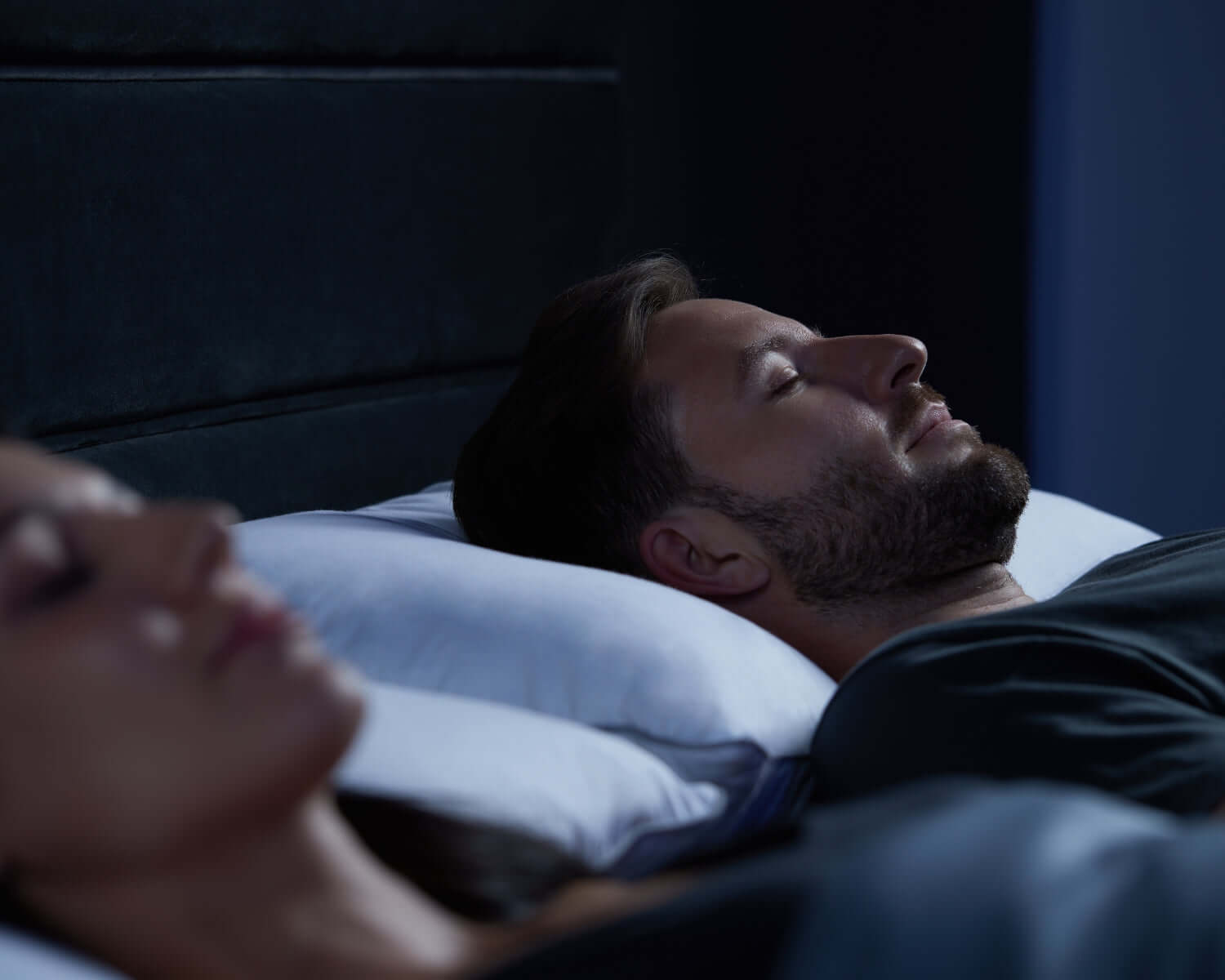 Man and woman sleeping peacefully on anti-snore pillows, demonstrating restful night's sleep solution.