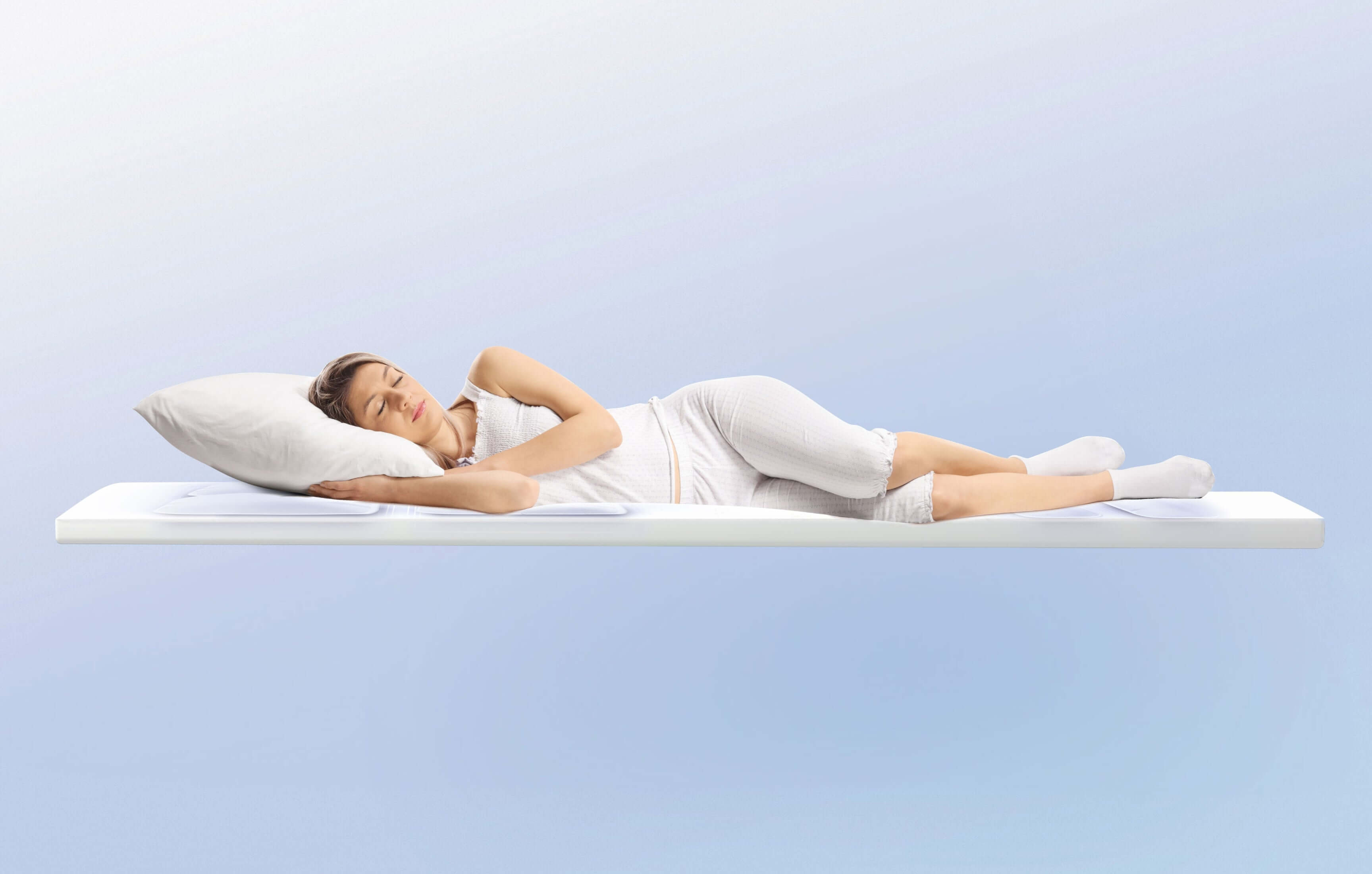 Woman peacefully sleeping on a white mattress against a soft blue background, demonstrating comfort and relaxation.