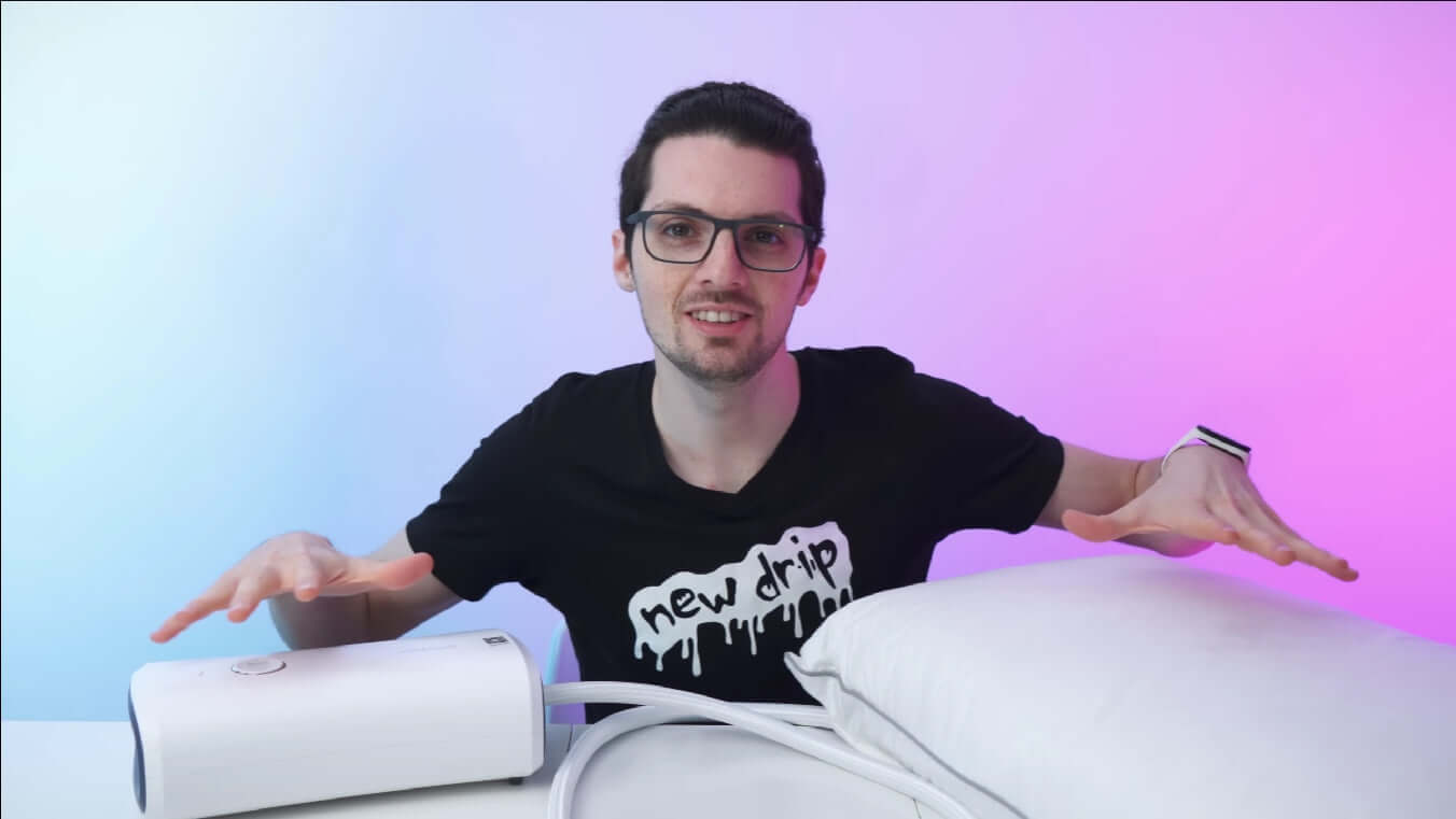 Person demonstrating a white technology device next to a pillow, highlighting modern product use against a colorful background.