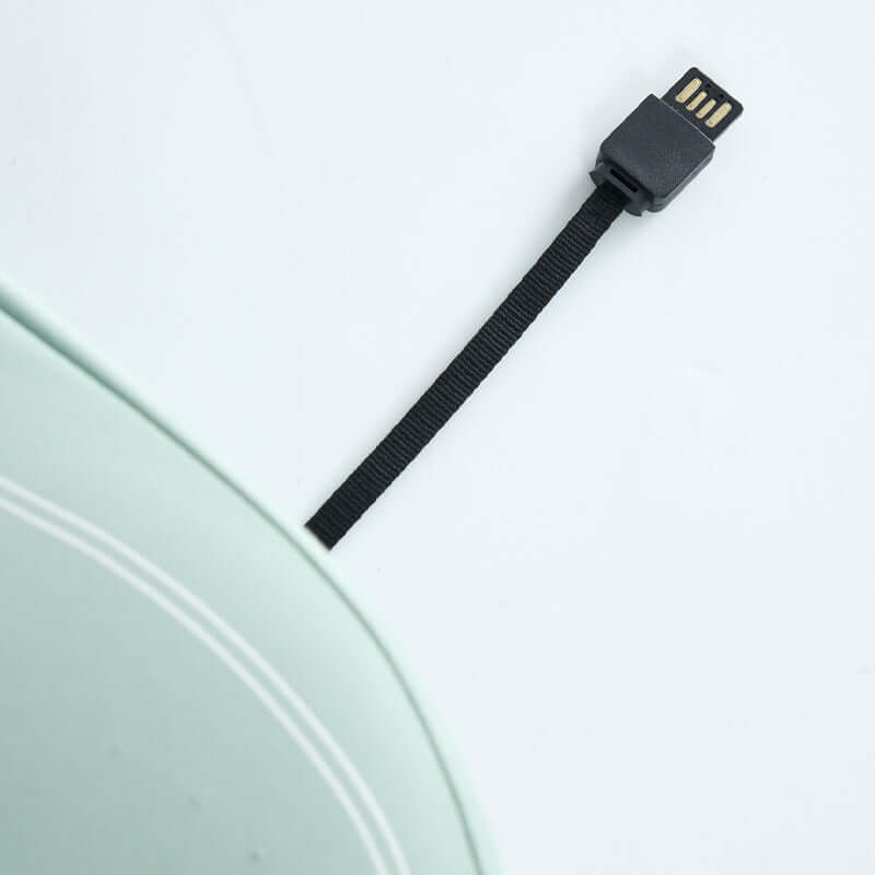 Close-up view of a USB cable lying on a white surface, next to a mint green laptop corner, for tech connections design concept.