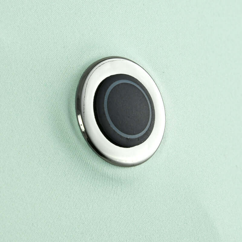 Close-up of a black and silver circular button on a light green surface, showcasing its smooth design and reflective finish.