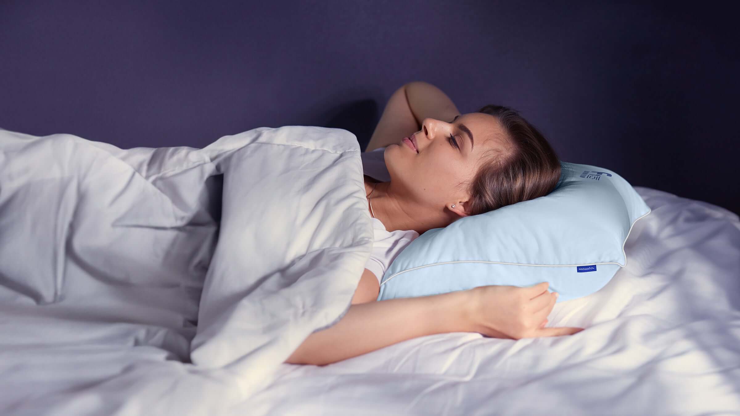 Woman sleeping comfortably on a white bed using a blue ergonomic pillow.