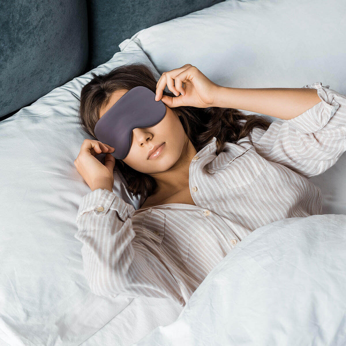 Woman wearing Nitetronic Sleep Mask in bed, showcasing ergonomic design for effective light blocking and improved REM sleep comfort.