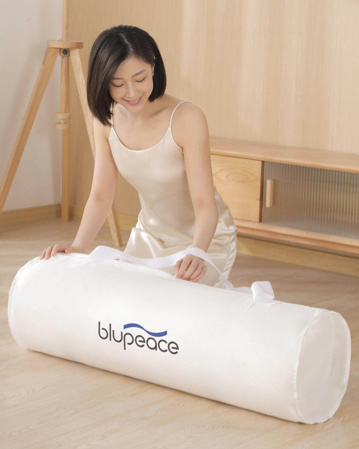 Woman unrolling Blupeace smart mattress pad indoors on wooden floor