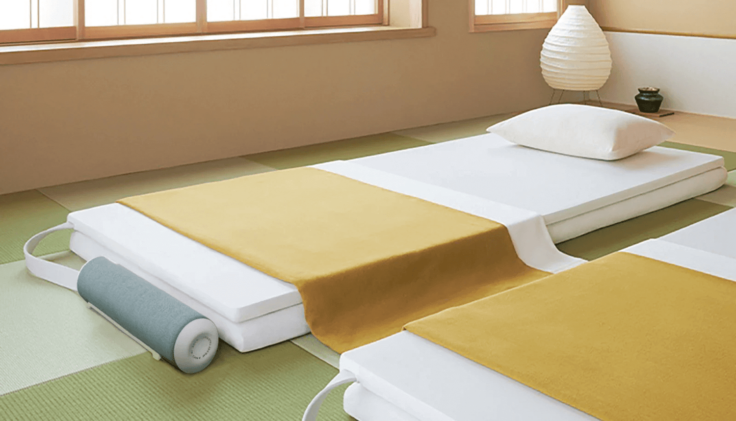 Minimalist Japanese-style bedroom with tatami mats and Nitetronic T3 Pro smart mattress pad featuring a yellow cover and cylindrical pillow.